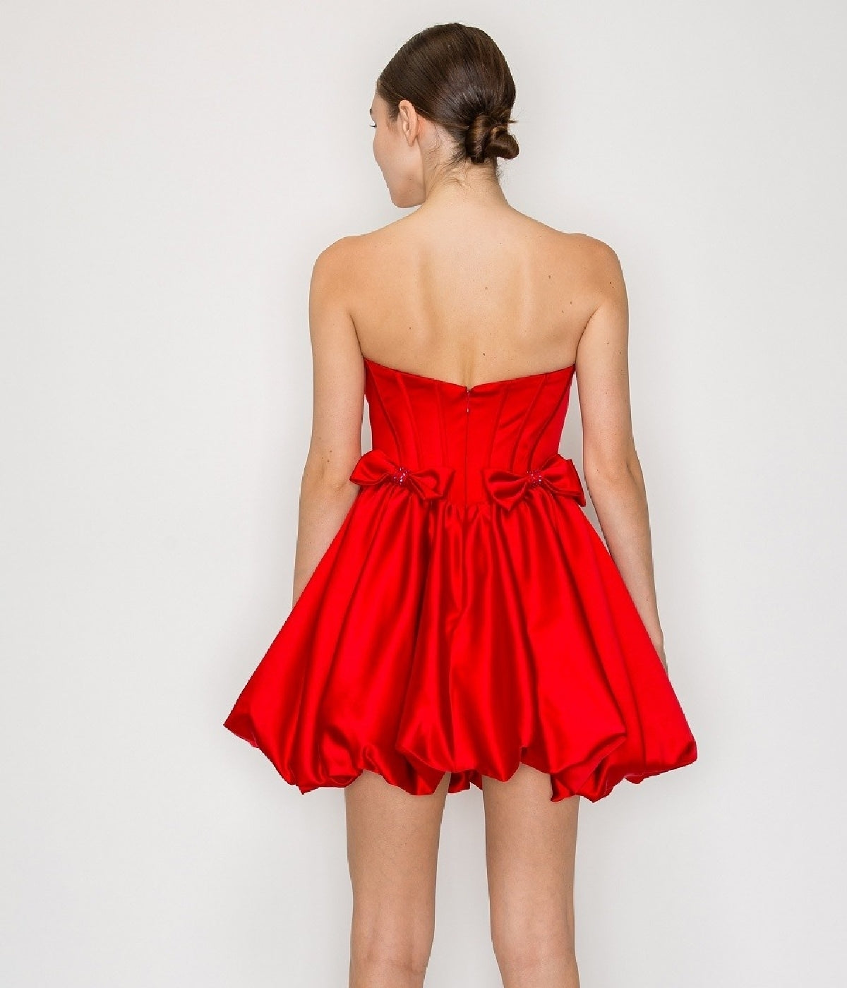 A woman faces away, wearing the Strapless Short Bubble Party Dress: Poly USA 9950 in bright red, featuring a bubble hem and bow details on the back.